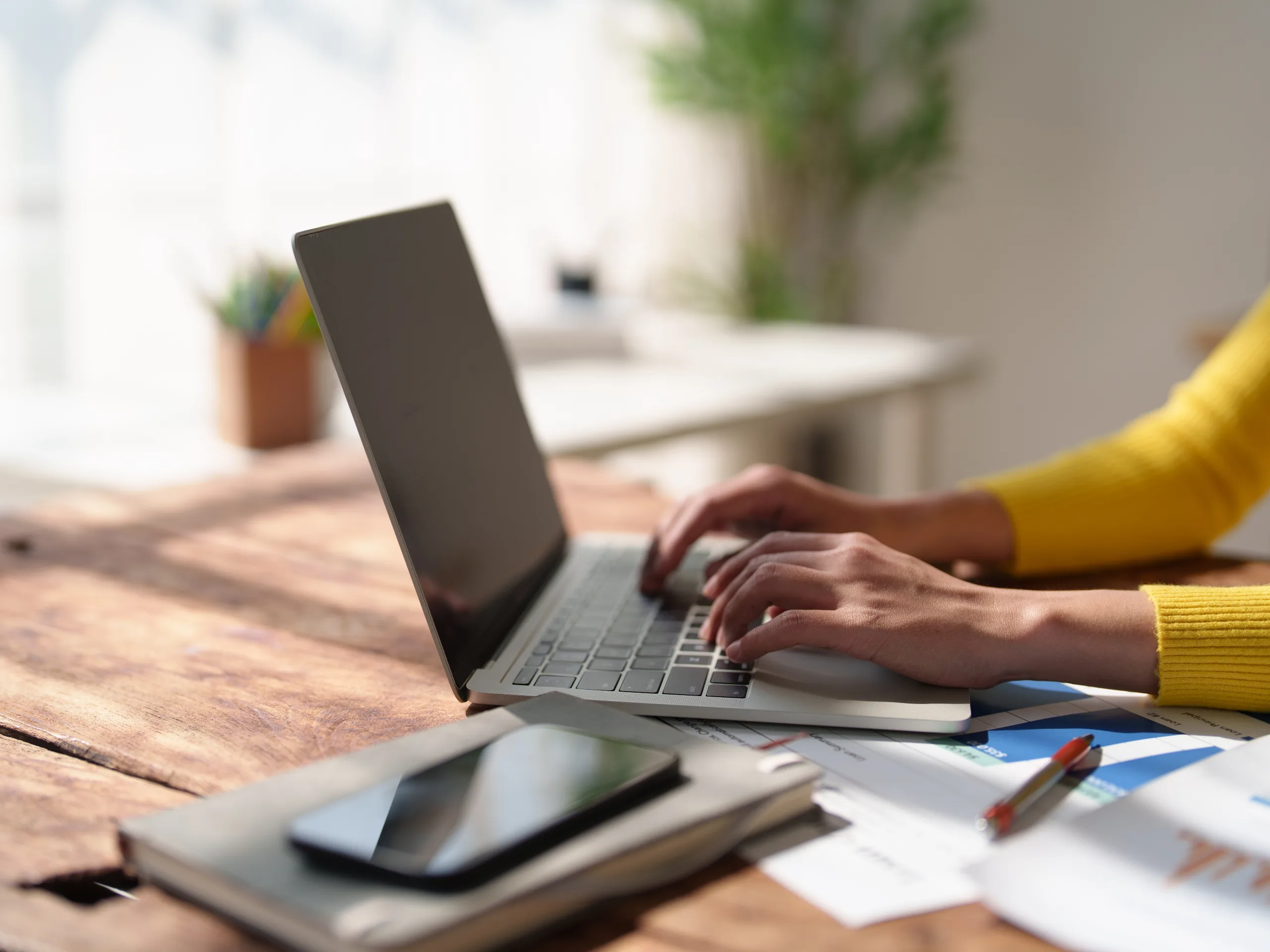 Person wearing a yellow sweater typing on a laptop